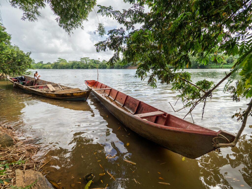 Wooden fishing boats resting by the lush banks of Rio Rama, Nicaragua, under a cloudy sky.